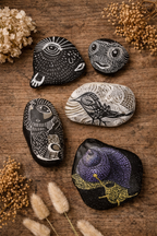 Black Big Fish Stone with a large white eye and radiating lines, displayed with other art stones and dried foliage on wood.