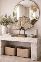 Textured, abstract wood decor piece on a dark stand with a rustic wood base, displayed on a marble console table.