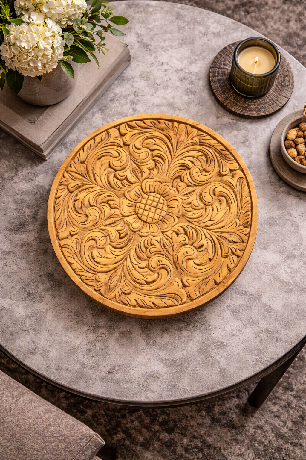 Round Nordic wood tray with an intricate floral carving, styled on a modern grey table with decorative items.