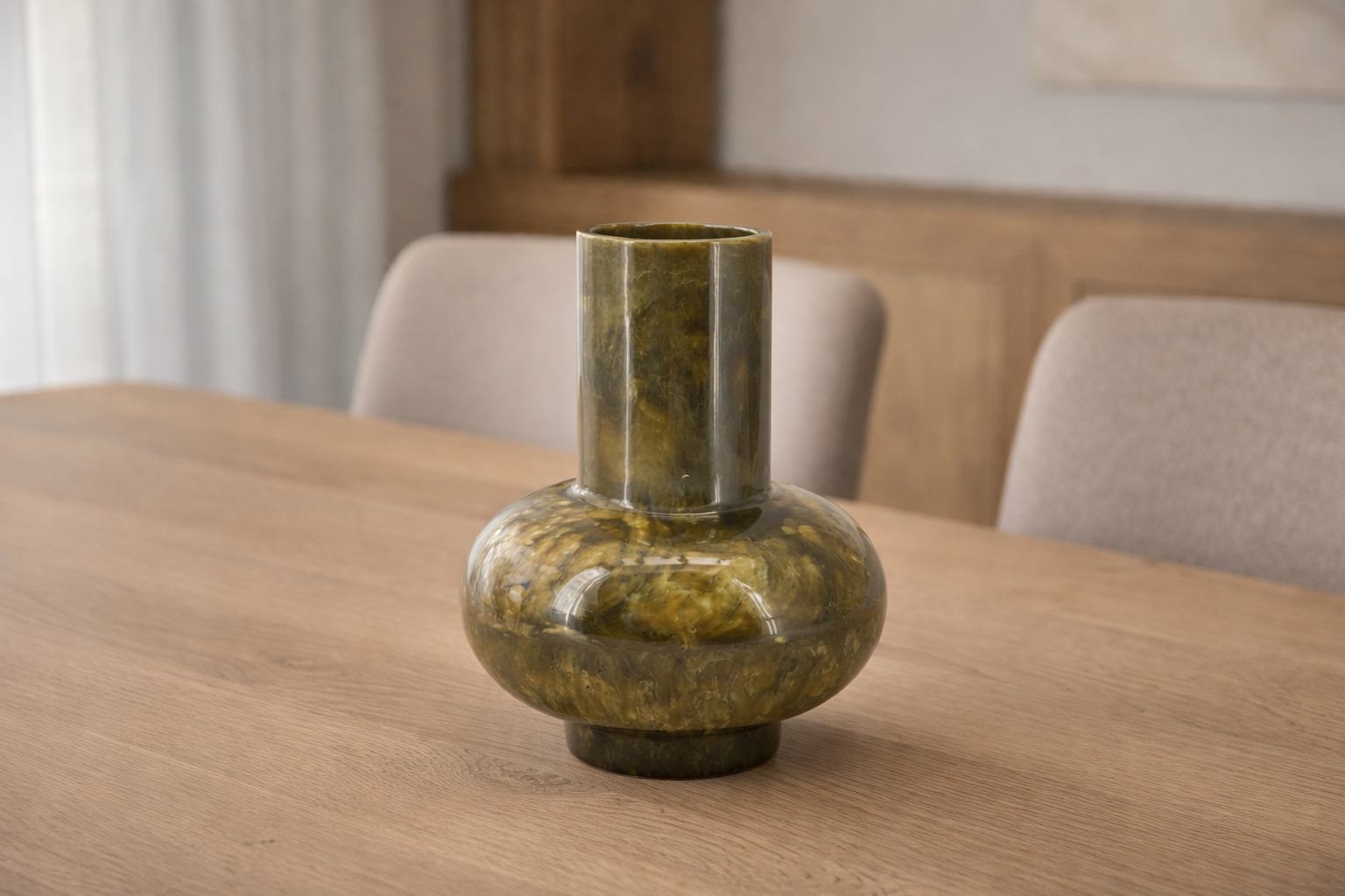 Green glass vase by Object and Story with a rounded body and cylindrical neck, sitting on a wooden table.
